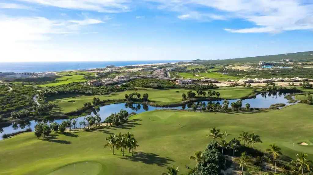Aerial view of Diamante golf course with water features, palm-lined fairways, residential neighborhoods, and Pacific Ocean coastline in the background