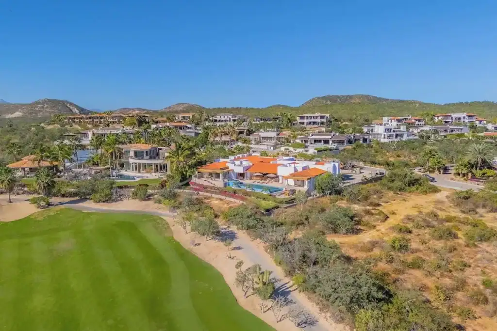 Aerial view of Puerto Los Cabos golf course residences with contemporary and Mediterranean-style homes, manicured fairways, palm trees, and the Sierra de la Laguna mountains in the background