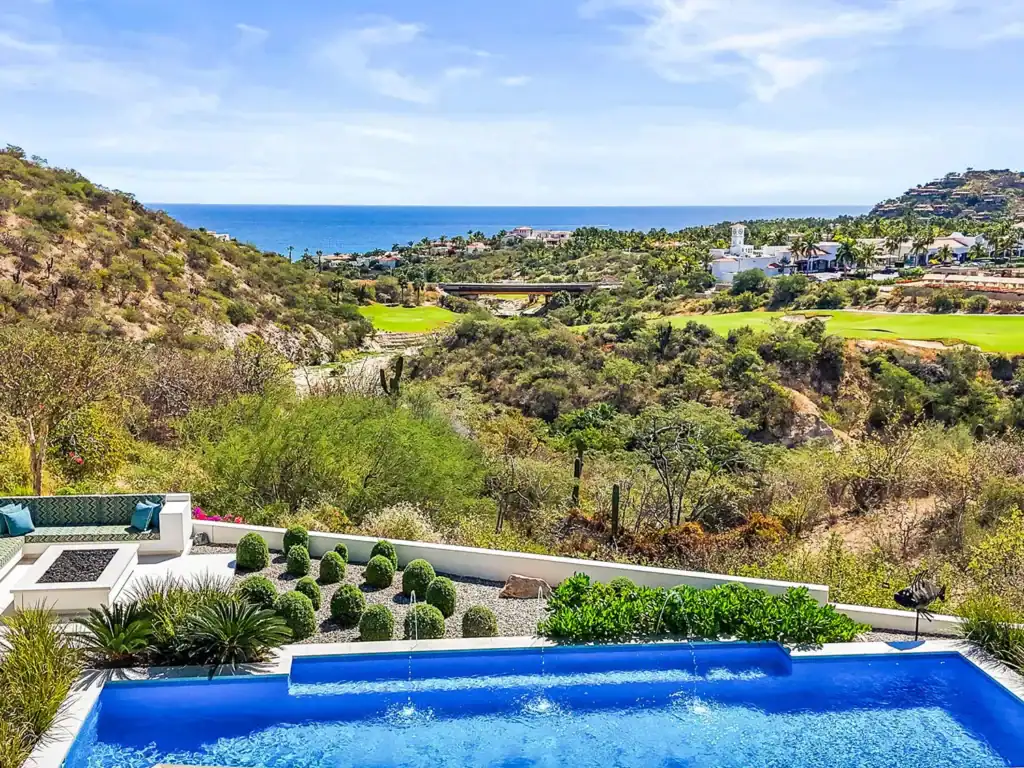 View from a Querencia residence terrace with infinity pool, built-in lounge seating, and landscaped garden overlooking the Tom Fazio golf course, clubhouse, and Sea of Cortez beyond desert arroyos