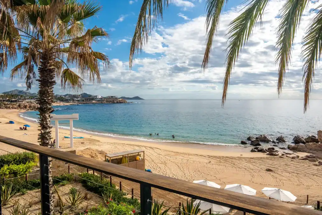 Chileno Beach protected cove with calm turquoise water, palm trees, beach umbrellas, and swimmers in the Sea of Cortez