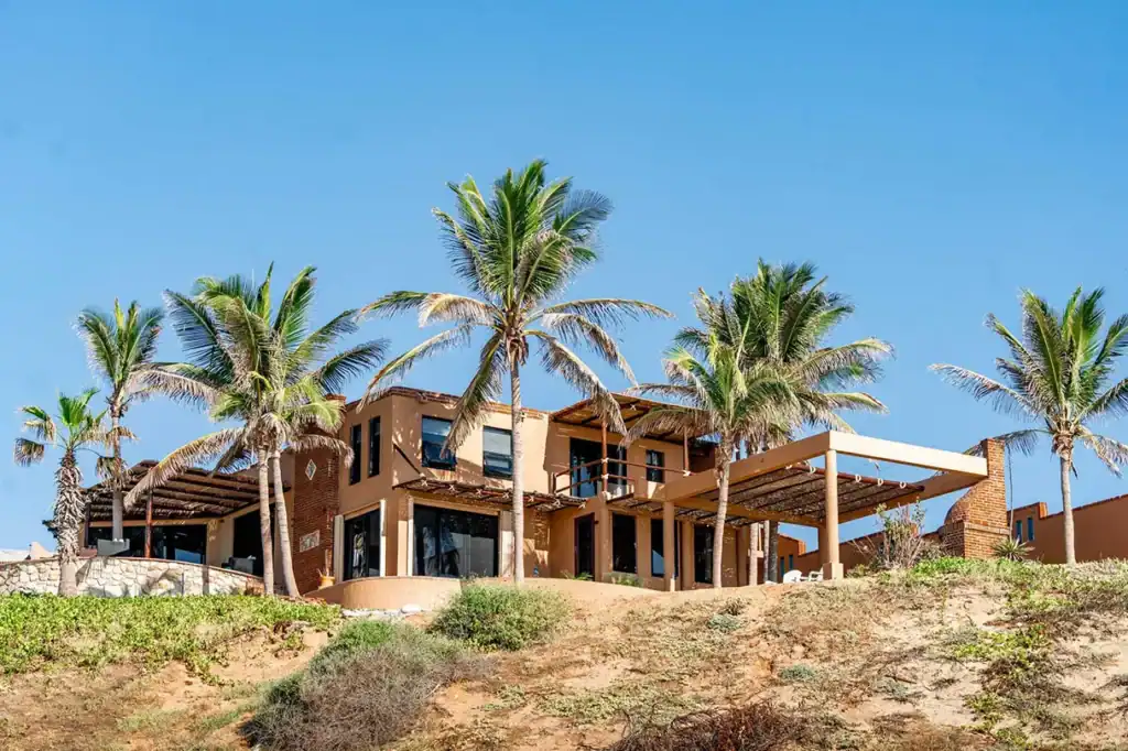 Beachfront villa with terracotta brick architecture and palm trees on a coastal dune overlooking the Sea of Cortez, East Cape, Baja California Sur, Mexico.