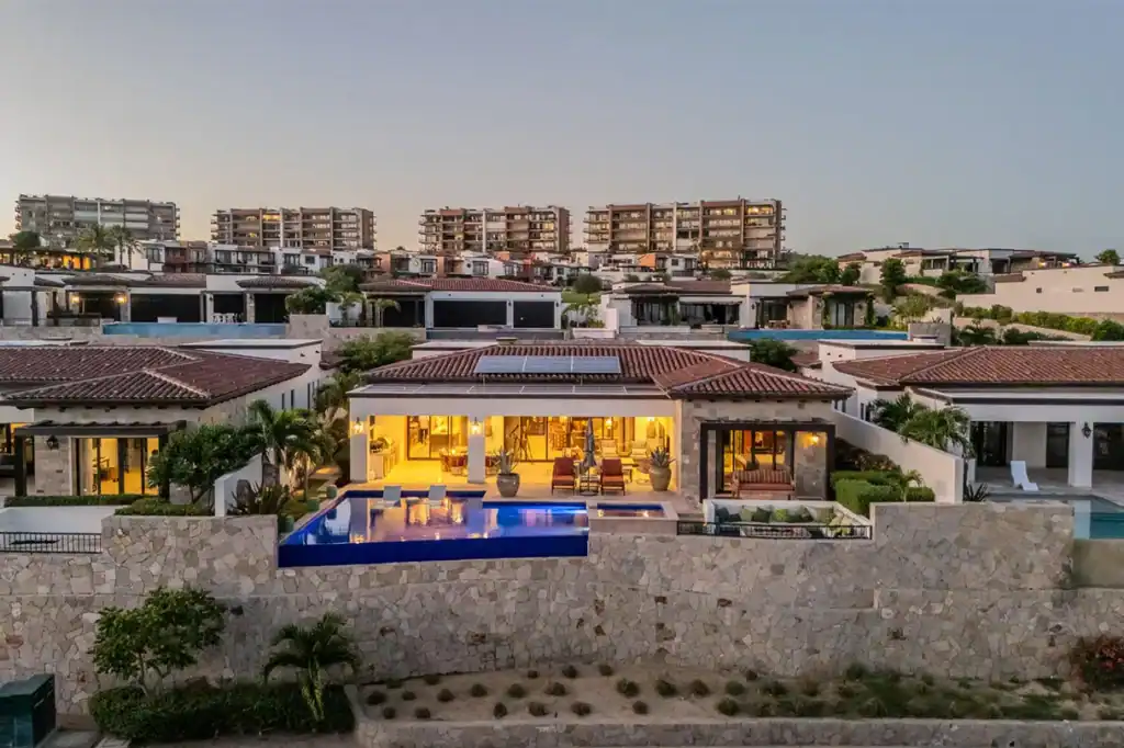 Luxury villa with private infinity pool and stone facade at dusk within a gated residential community on the Pacific side of Los Cabos, Baja California Sur, Mexico.
