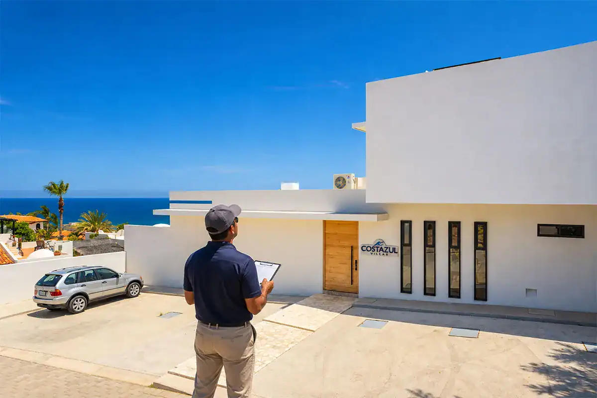 Appraiser with a clipboard outside a white modern home with an ocean view during an avalúo in Los Cabos